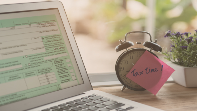 laptop with alarm clock and post it note that says tax time